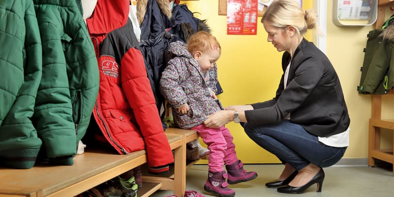 Die „Bildungsmisere“ – die Kita soll es richten, Kind und Frau im Eingangsbereich der Kita