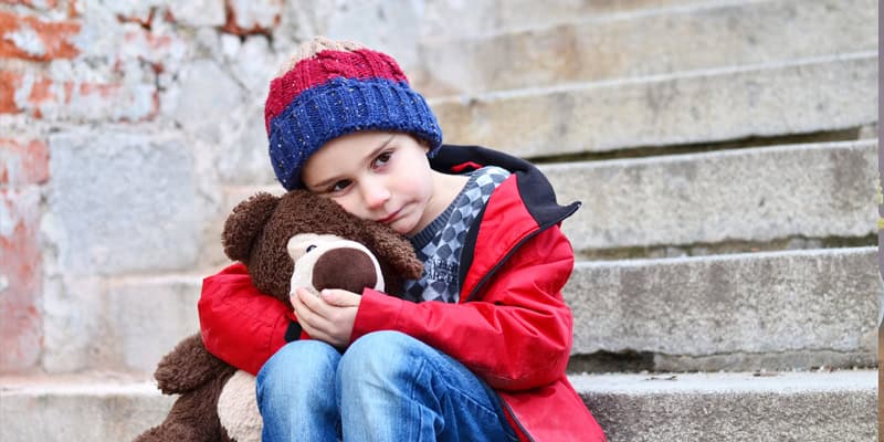 Kinder im Trauerprozess unterstützen, Kind sitzt mit Teddybär auf einer Treppe und ist traurig