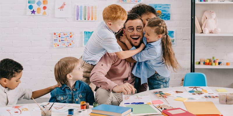 Männlicher Erzieher wird von Kindergartenkindern umarmt