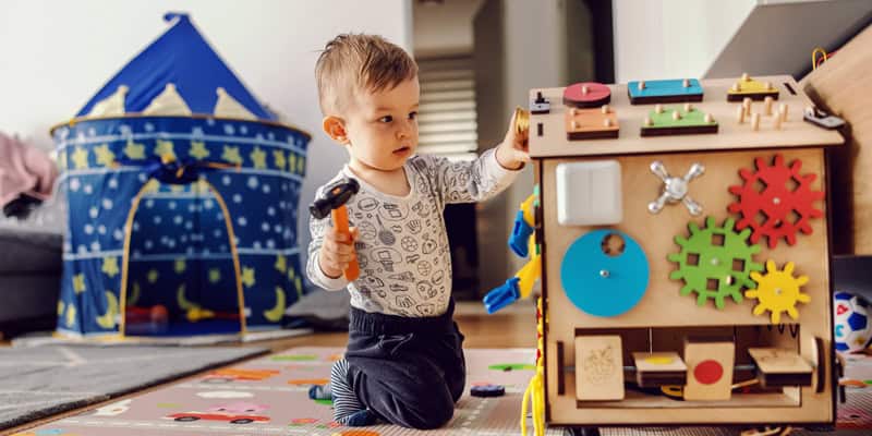 Projekte oder freies Spiel in der Krippe? Kleinkind hämmert an Spielzeughaus